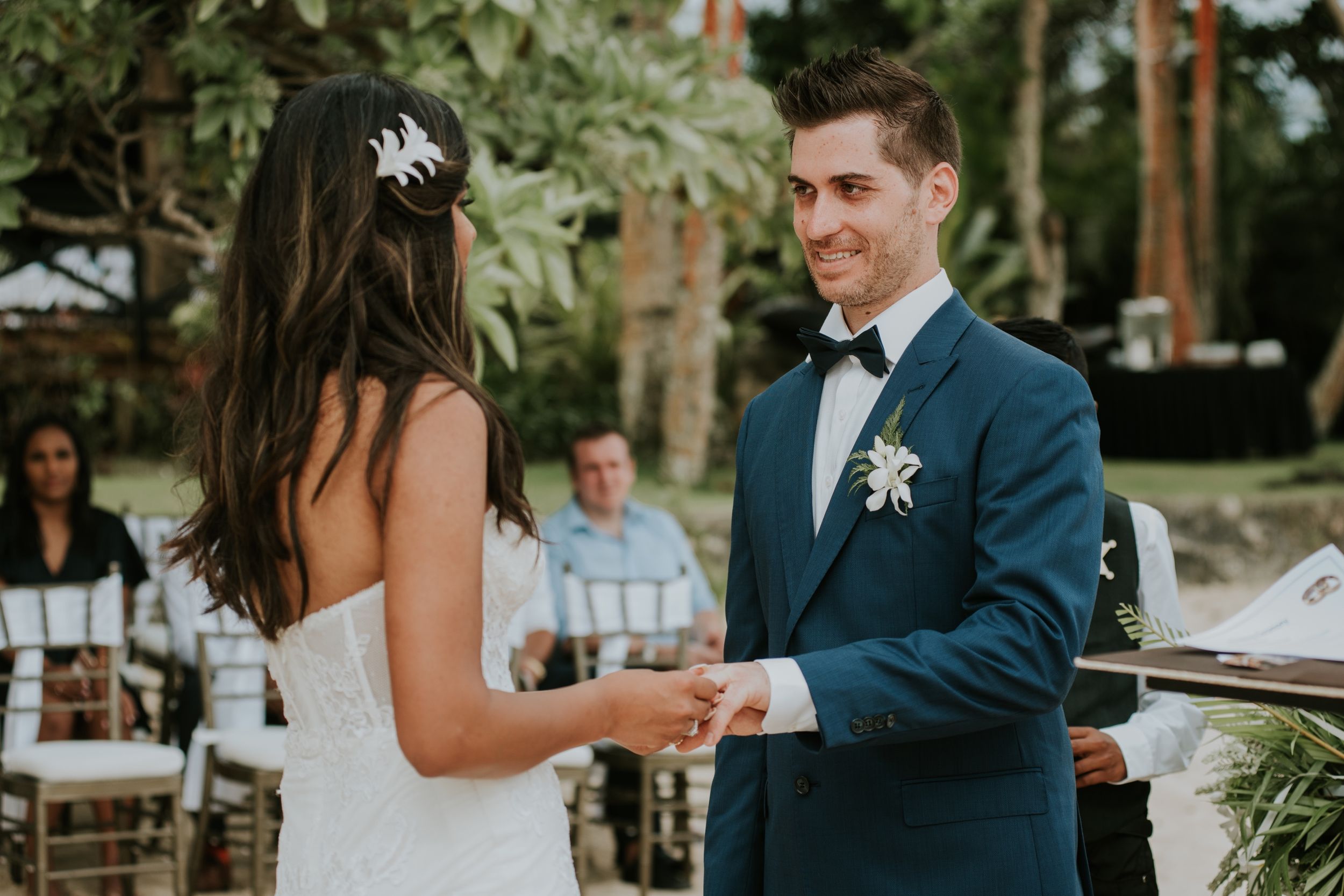 Couple holds hands during their outdoor wedding ceremony under palm trees.
