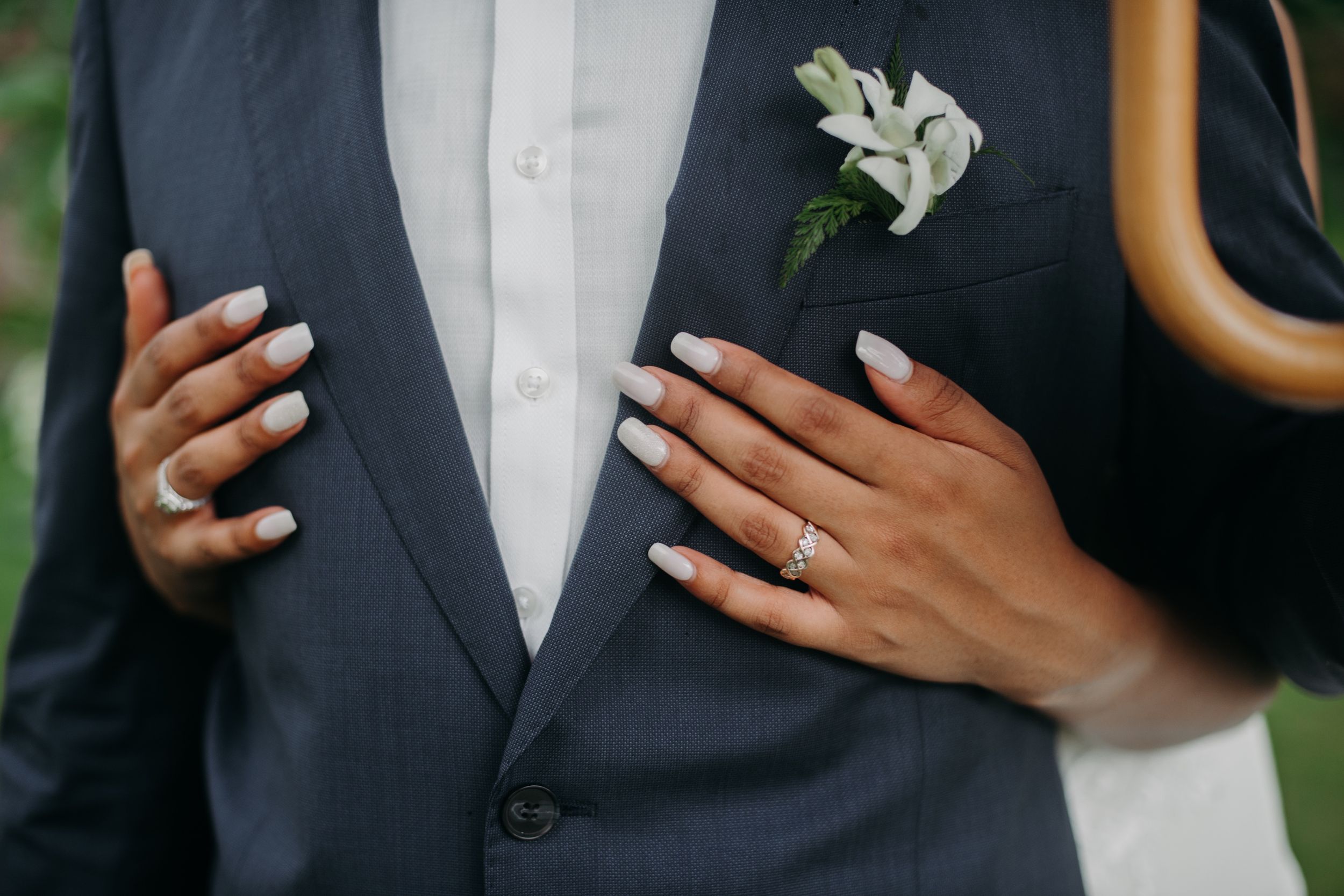 Close up of hands on a navy suit jacket with white boutonniere.