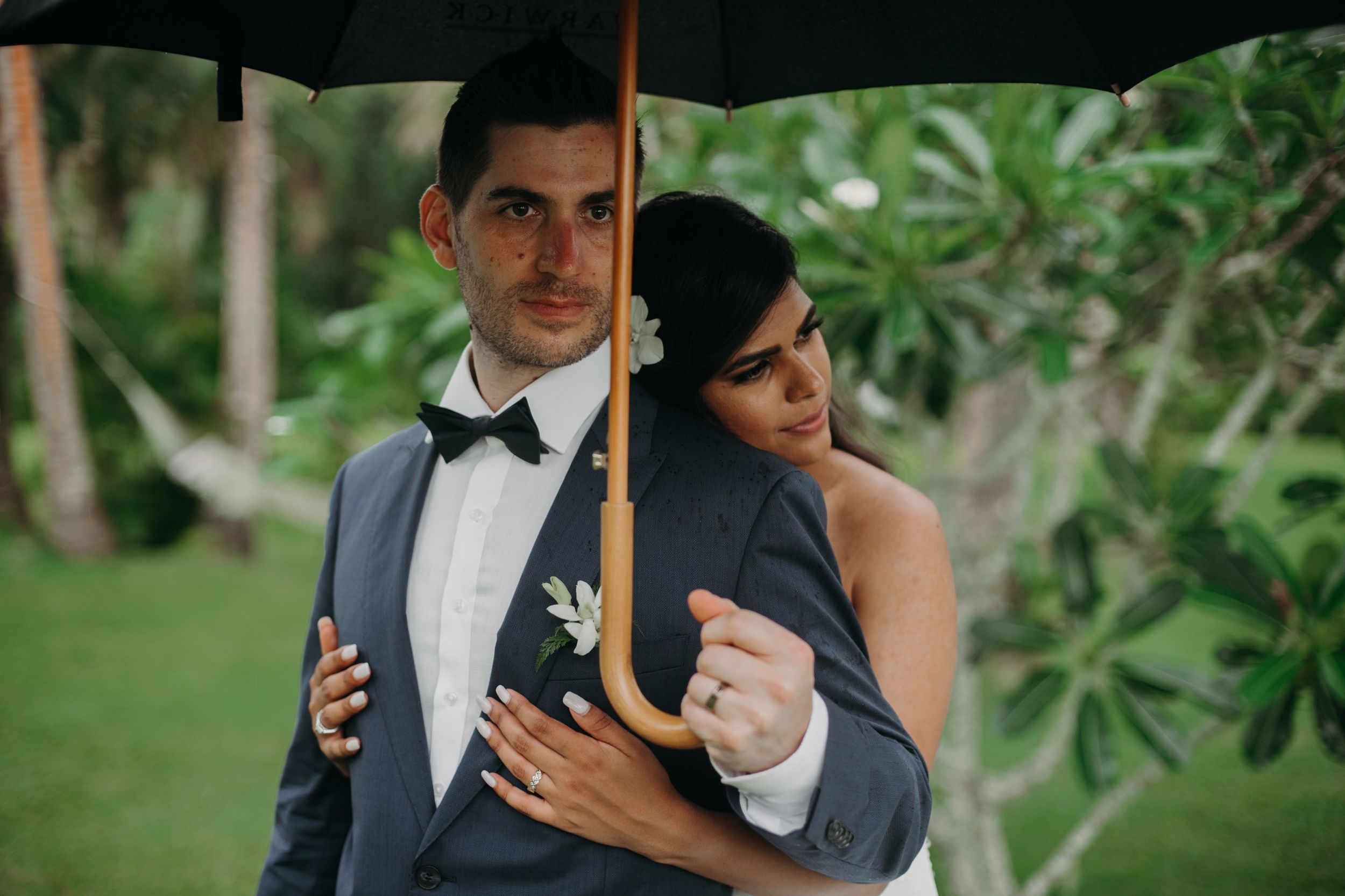 Couple embracing under black umbrella in lush tropical garden setting.