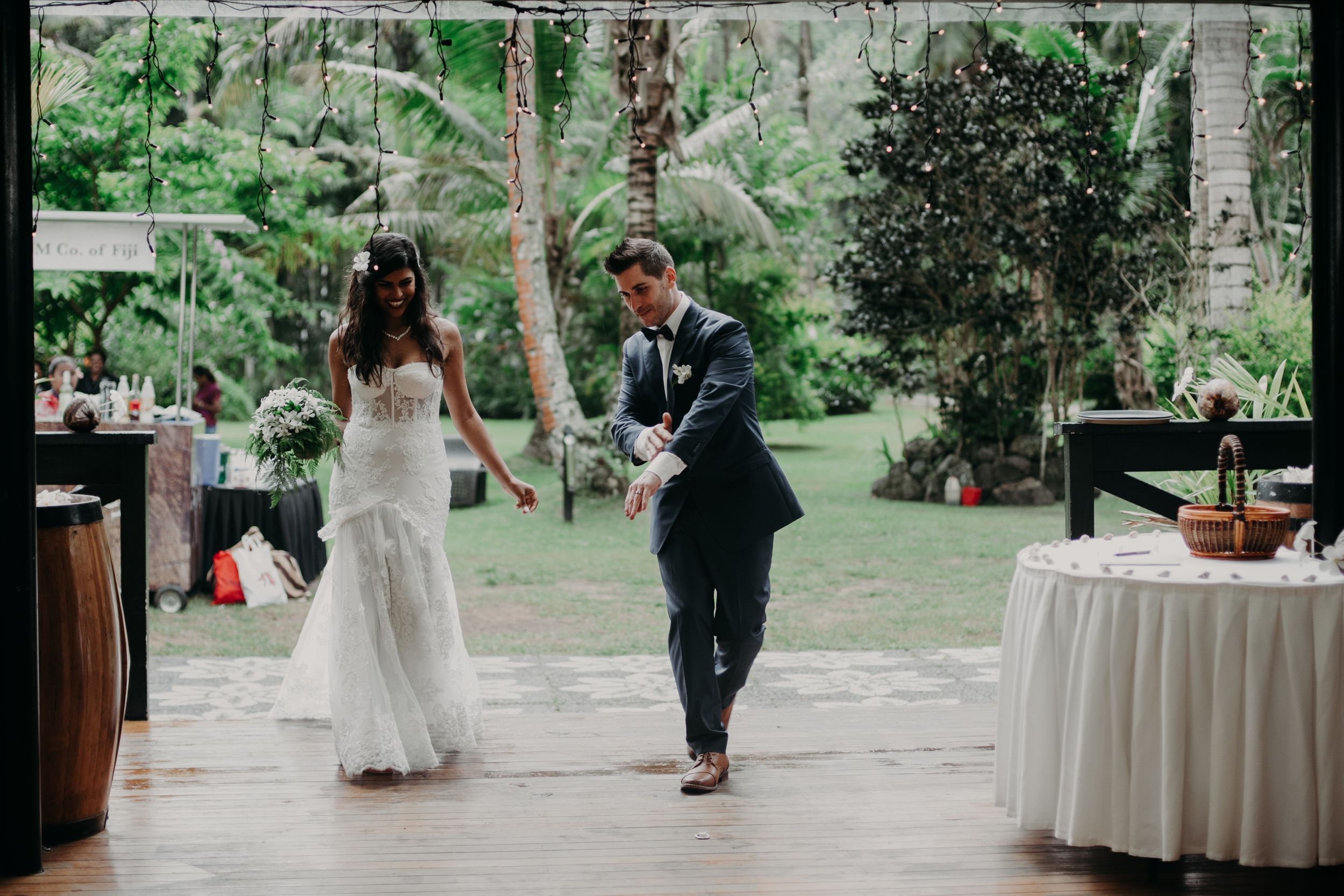 Reception venue with wooden beams and white tables set against a lush tropical garden backdrop.