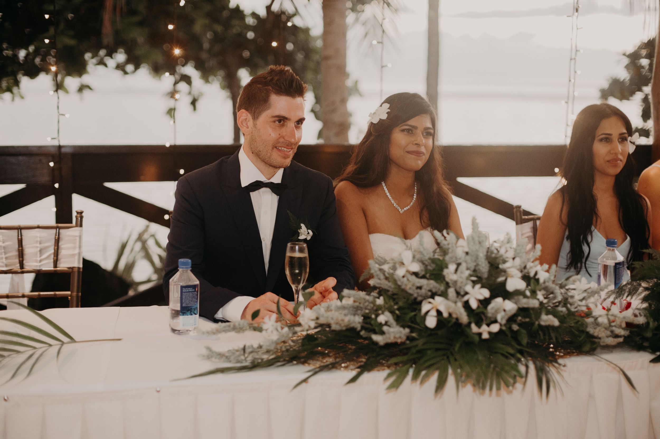 Wedding party seated at head table decorated with lush greenery garland.