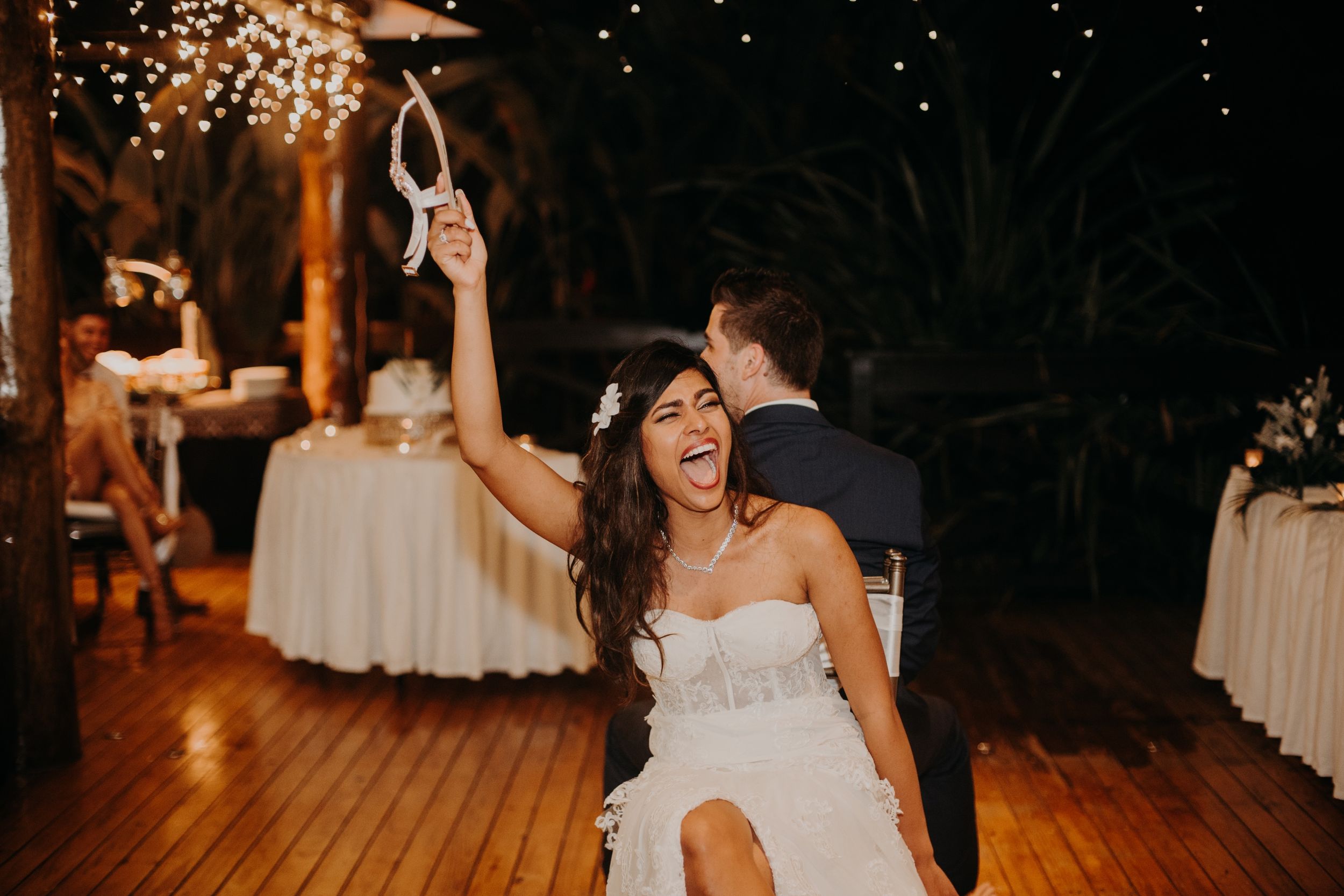A joyful dance moment at a wedding reception with twirling under warm string lights and white decor.
