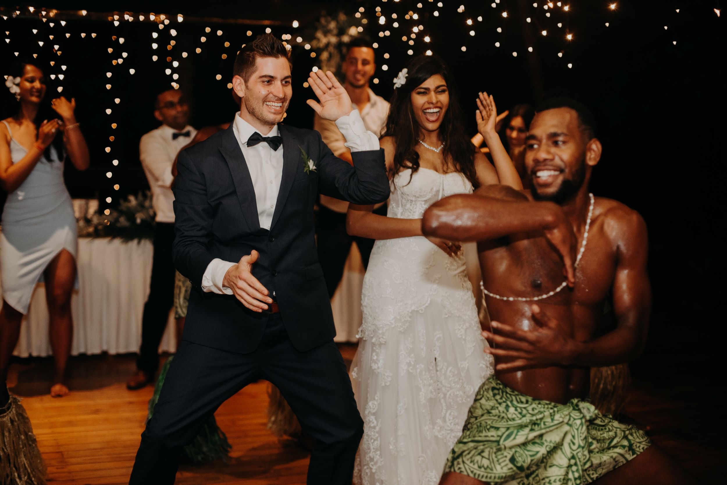 Wedding guests dancing enthusiastically on a wooden dance floor under twinkling lights.