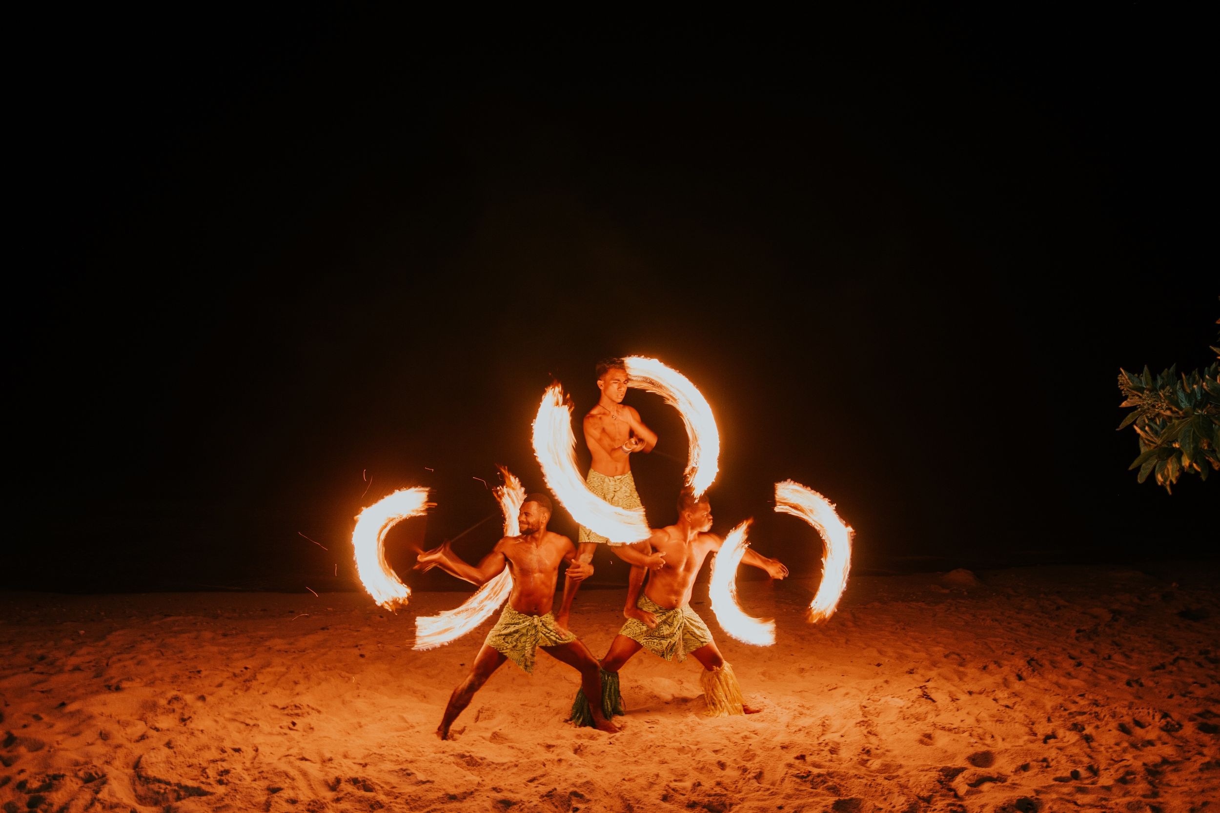 Fire performers creating spectacular light patterns on a sandy beach at night.