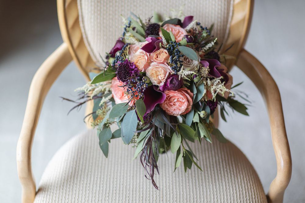 Wedding bouquet with pink roses and purple flowers arranged on vintage chair.