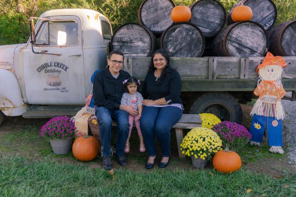 Family posing with fall pumpkins and barrels at Cobble Creek Distillery on an autumn day.