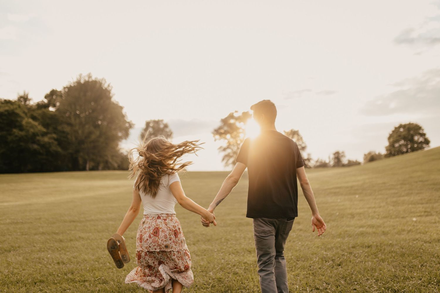 Couple runs playfully through a sunlit meadow at golden hour.