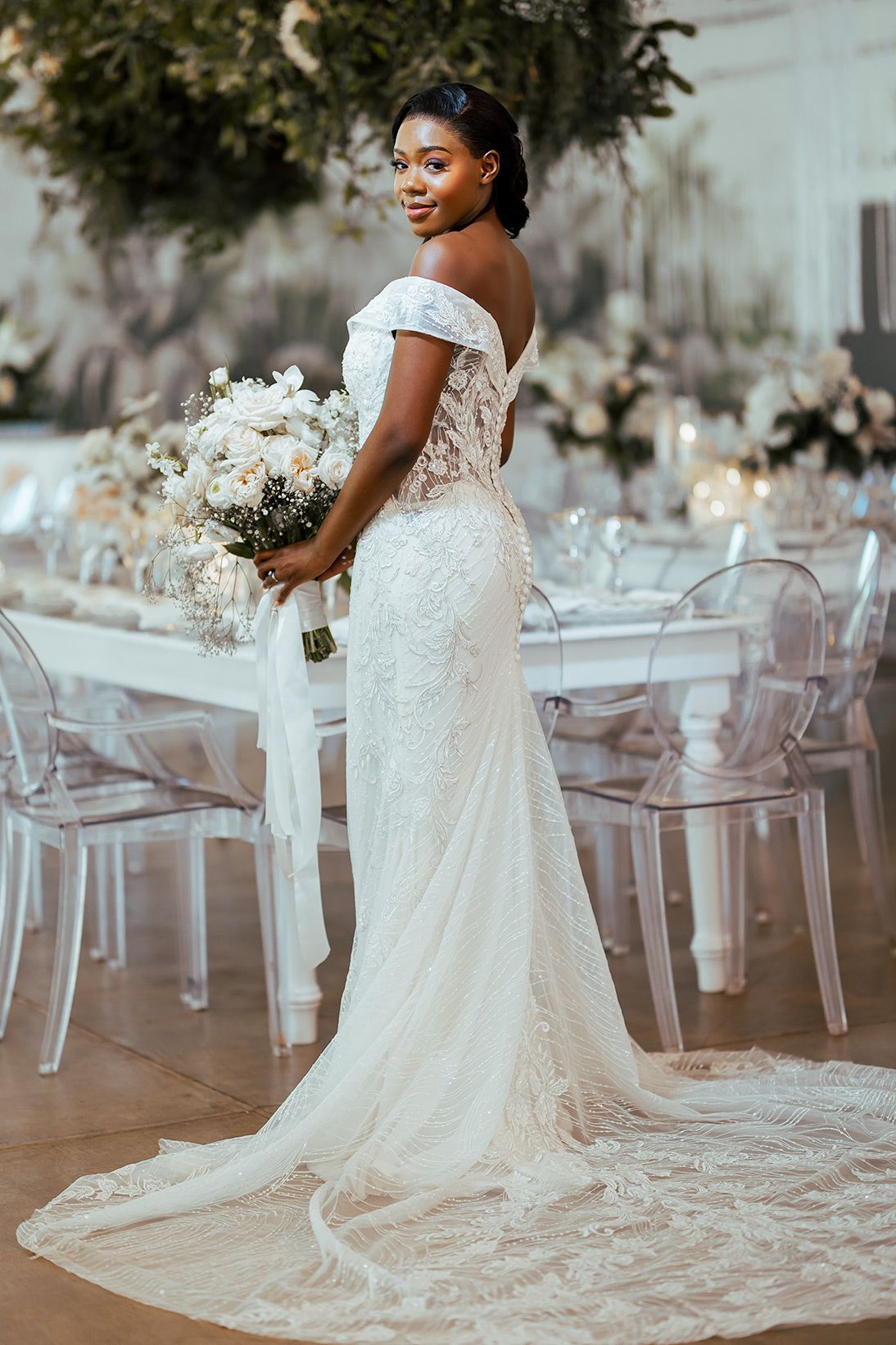 Elegant off-shoulder lace wedding gown with long train showcased in a modern reception venue.