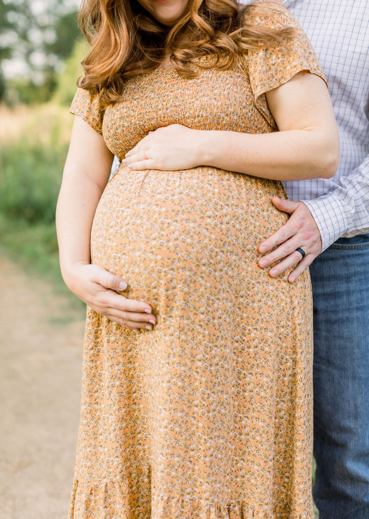 Close-up detail of hands cradling a pregnant belly in a peachy floral dress.