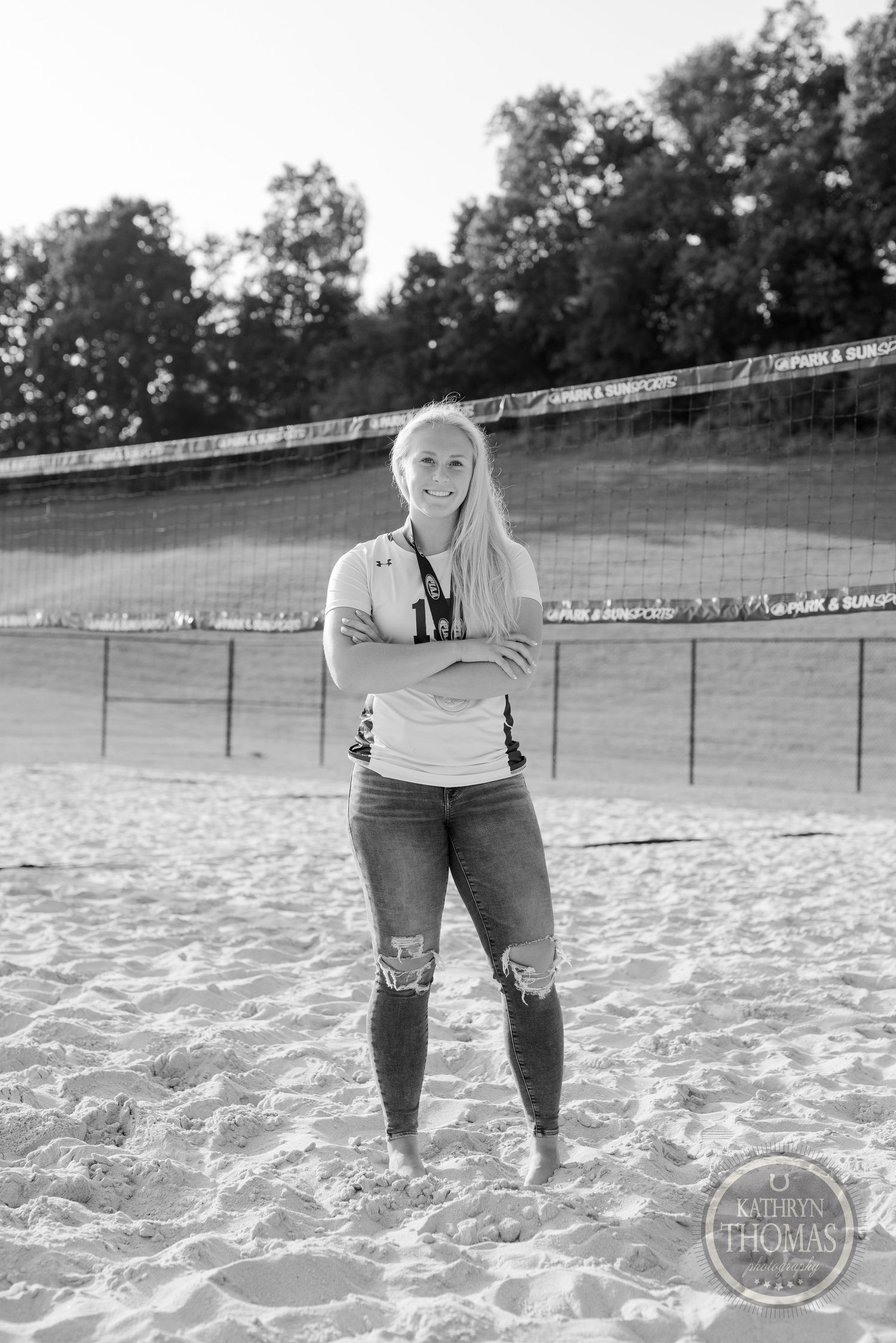 Black and white portrait of athlete standing on beach volleyball court with nets visible.