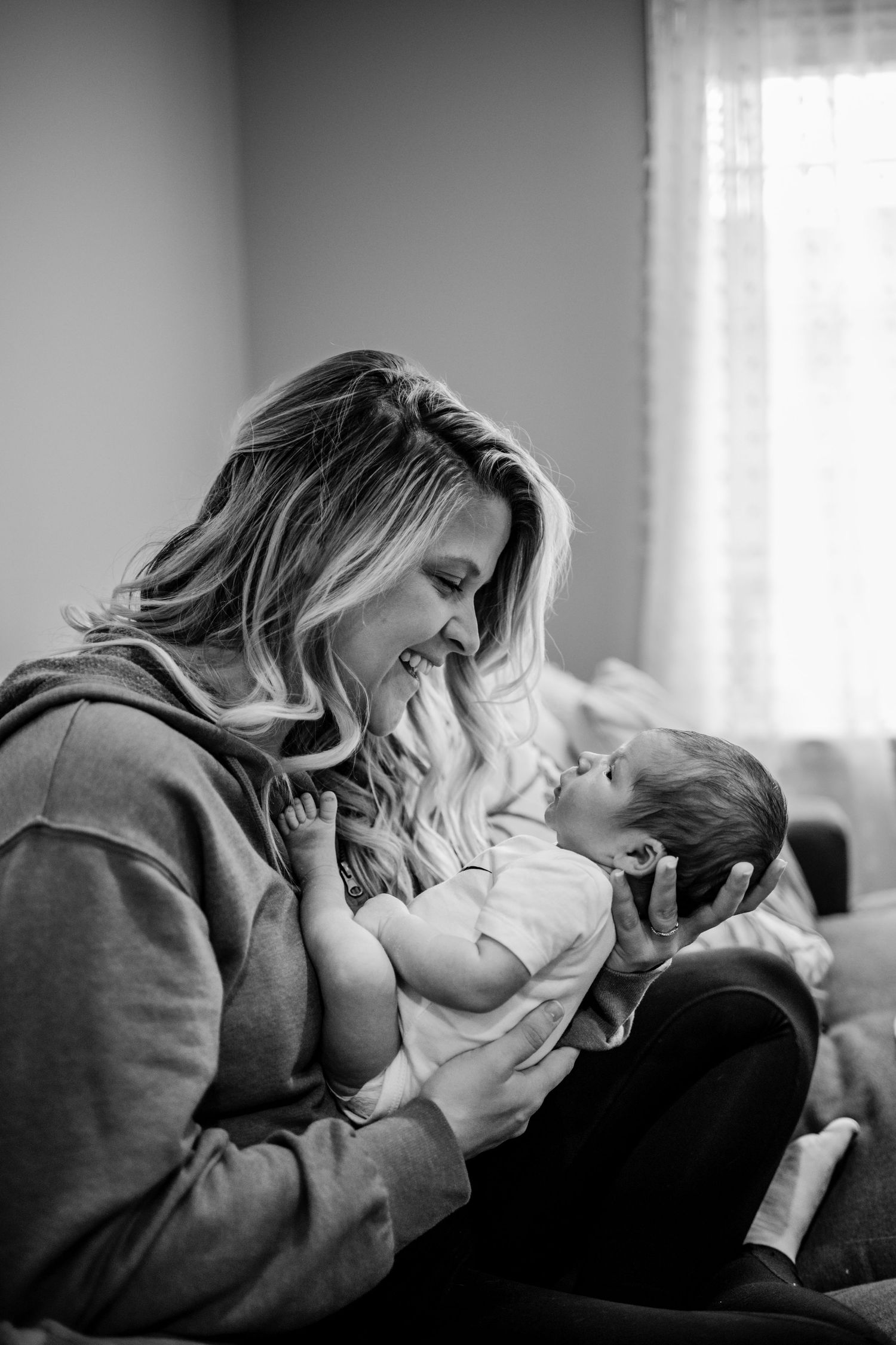 Intimate black and white photo of tender moment between parent and newborn on couch.