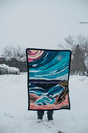 Art memory quilt called 'Susseration of the soul' being held up with snow in the background.