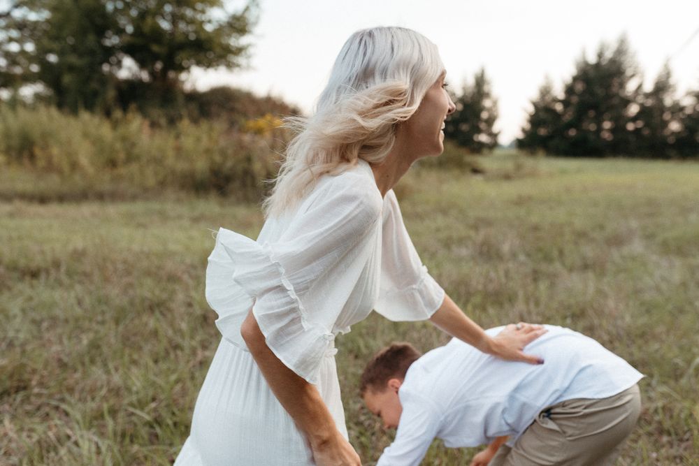 Playful interaction between two people in white outfits in a grassy field.