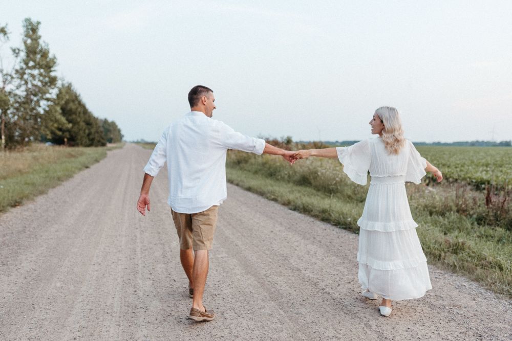 Couple walking apart while holding hands on rural dirt road.