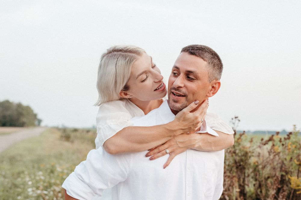 Playful couple embracing and laughing together in outdoor field setting.