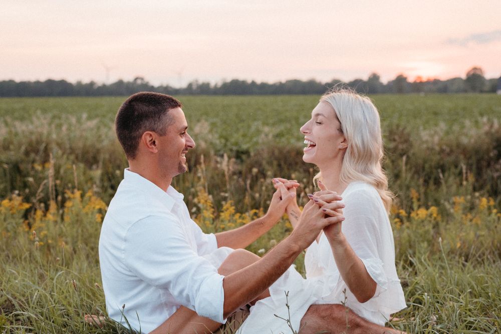 Couple sharing joyful moment while sitting in wildflower field at sunset.