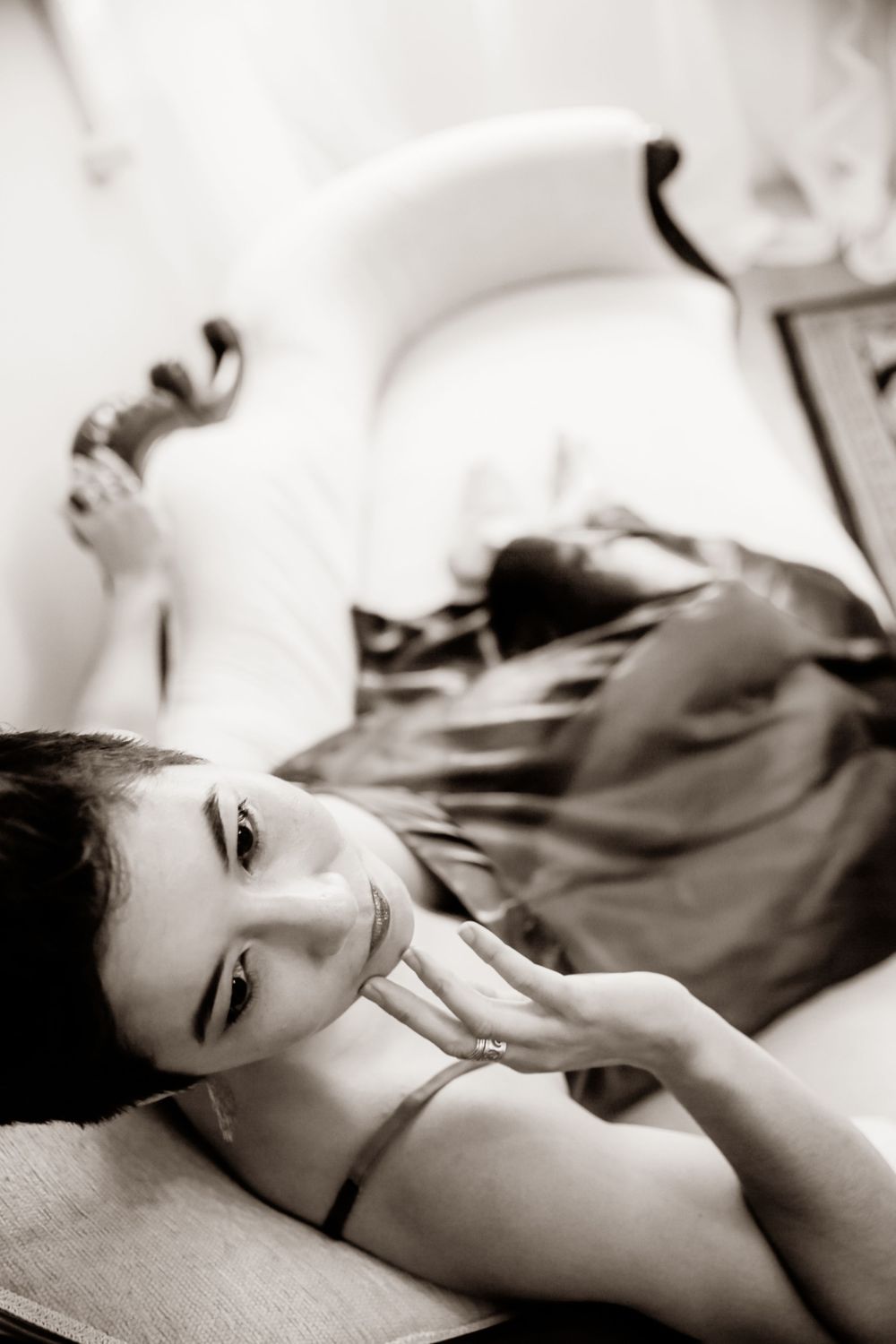 A black and white boudoir portrait showing artistic pose on white bedding.