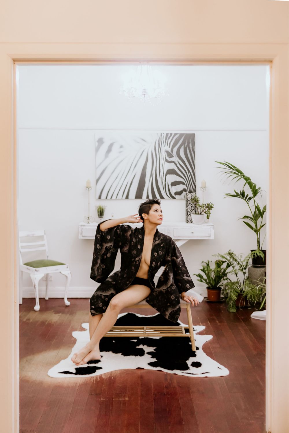 Artistic portrait in black robe with zebra artwork and plants in bright white studio setting.