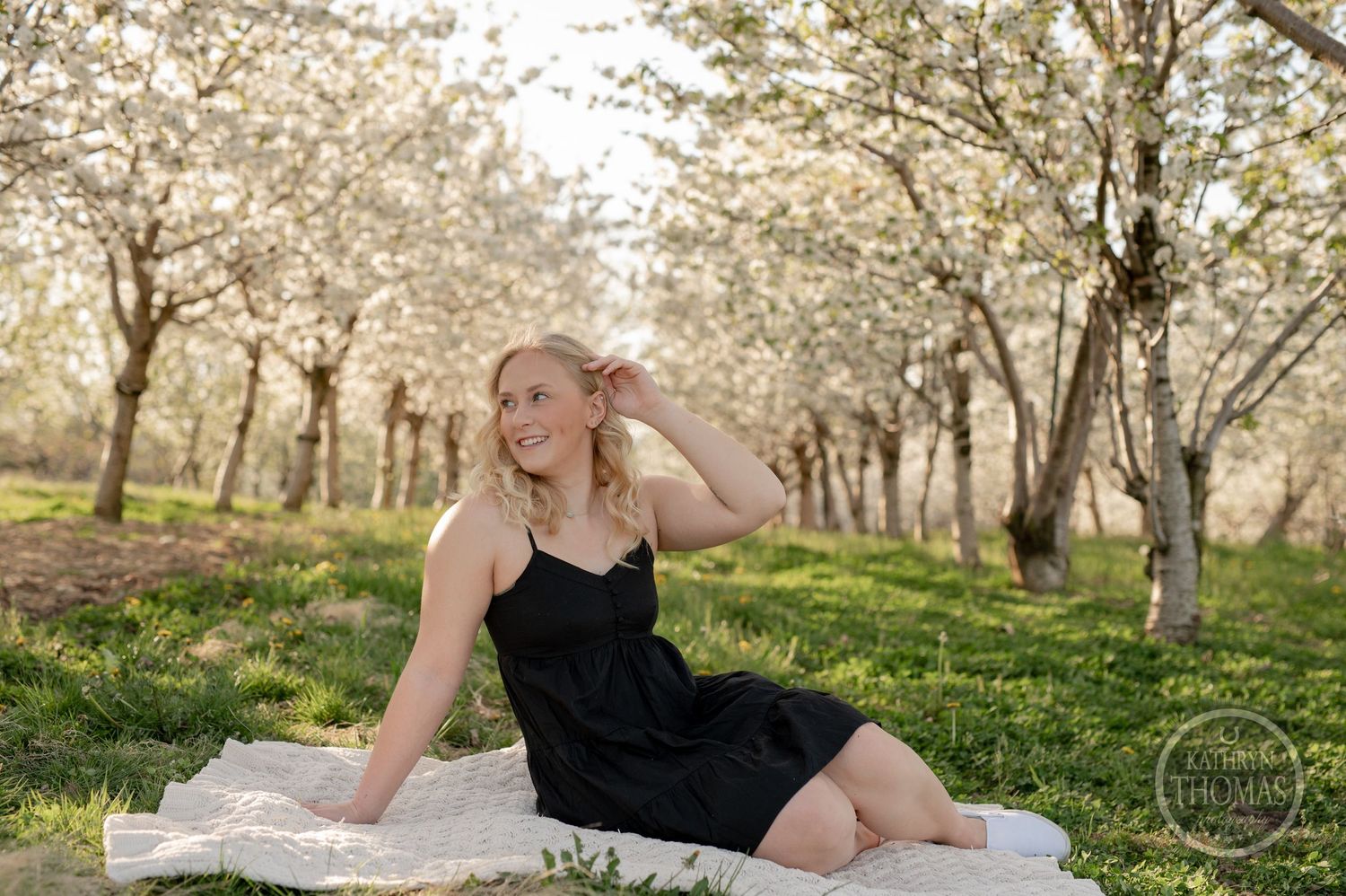 Springtime outdoor photography session on white blanket surrounded by blooming trees.