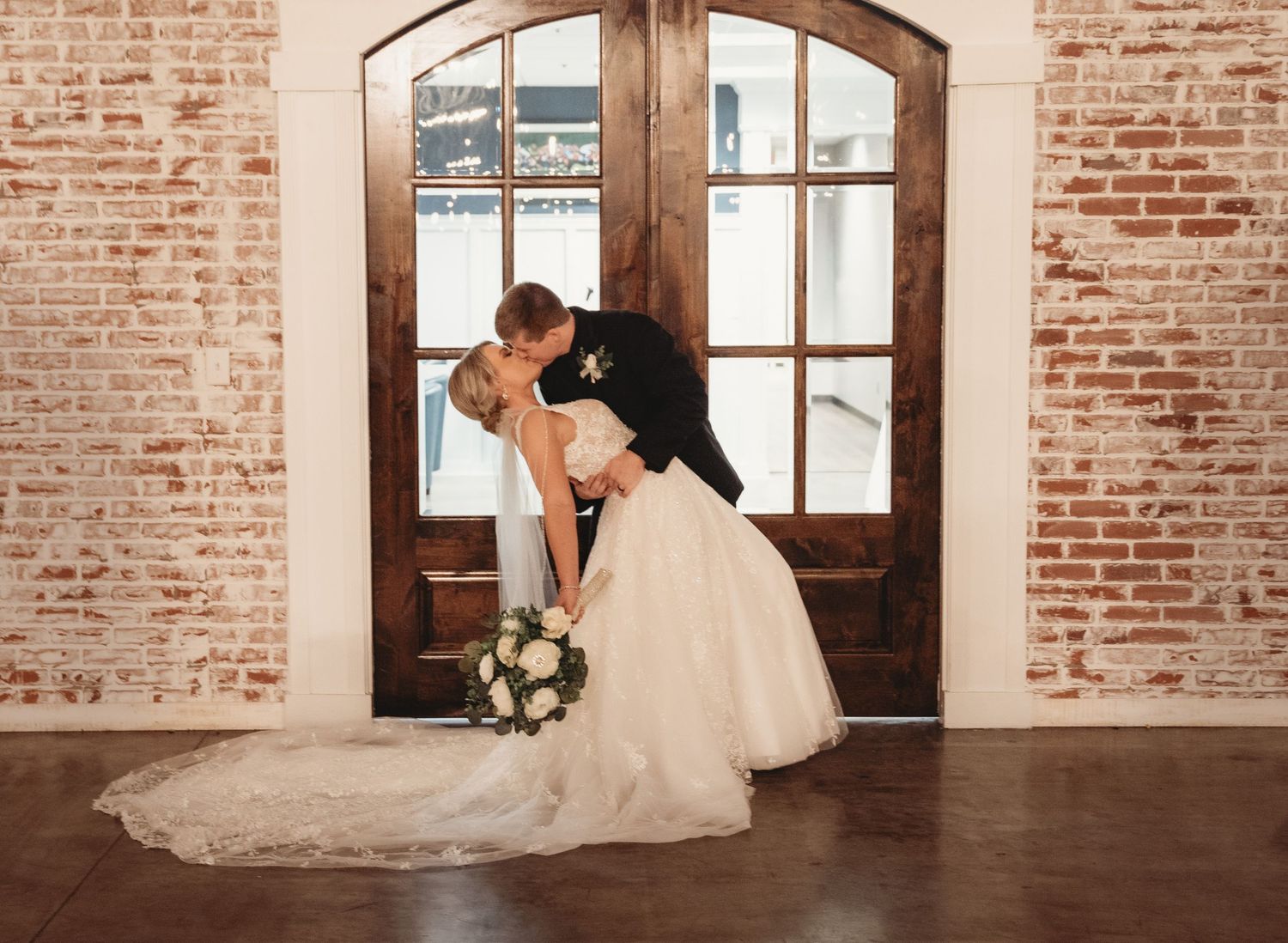 Wedding couple dancing in rustic brick venue with sunlight streaming through windows.