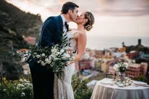 Bridal couple sharing a kiss at the epic view of cinque terre in Italy during a cotton candy sunrise with a sweetheart table.