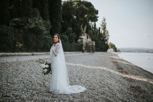 Bridal portrait of a bride with a veil holding florals on the rocky lake coast of Sirimione, Italy.