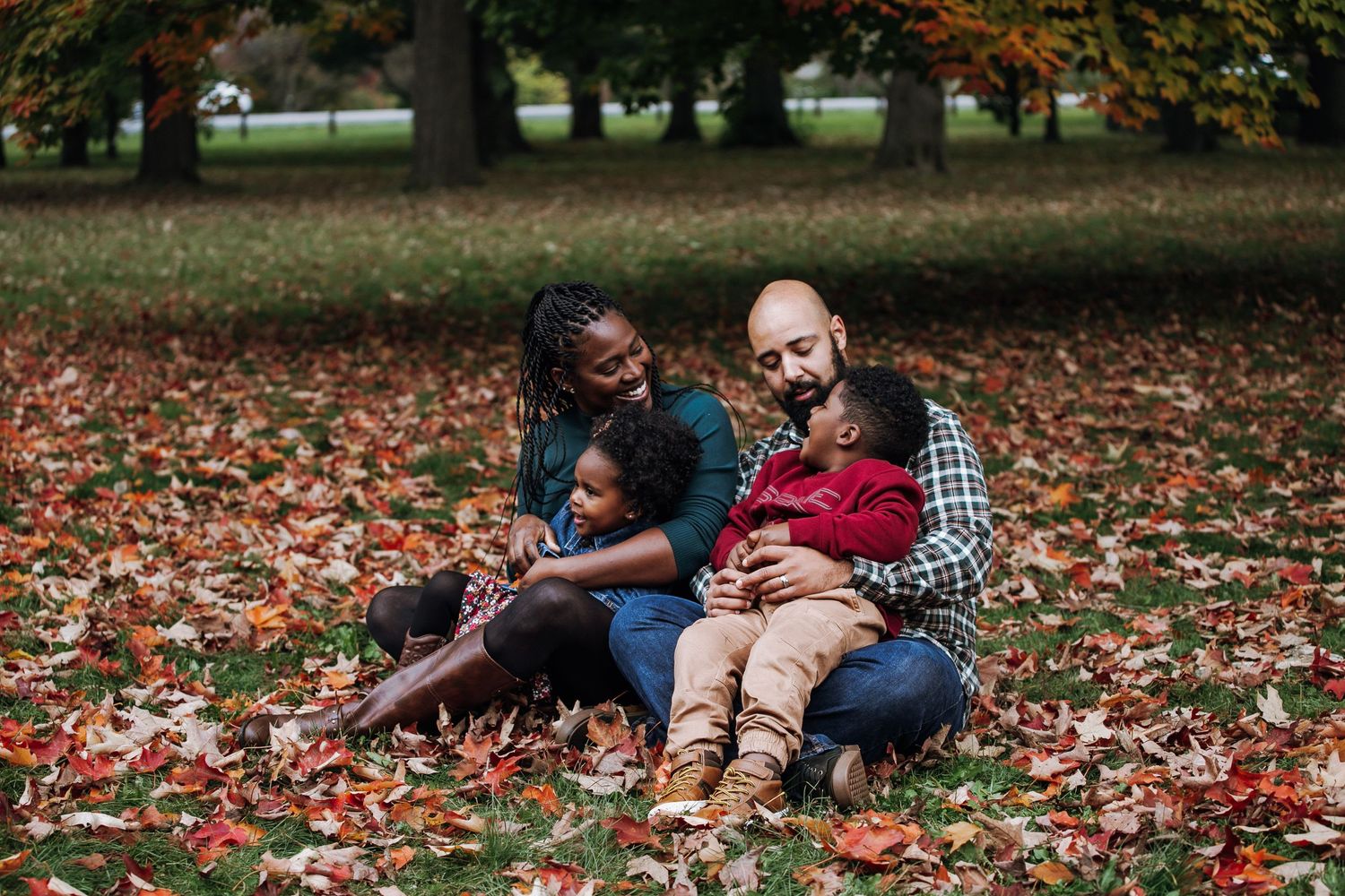A couple sits together on autumn leaves in a park sharing a lighthearted moment.