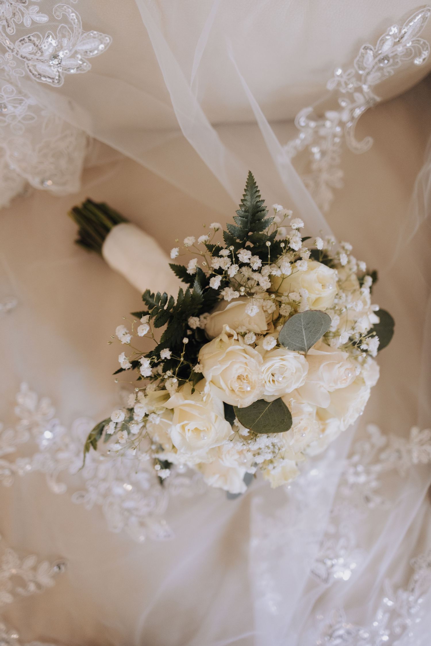 An elegant white rose wedding bouquet with greenery and baby's breath on lace.