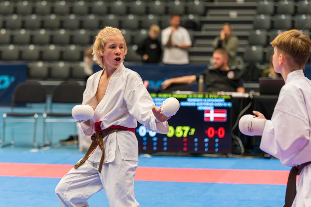 Female karate competitor in brown belt throws punch during tournament match on blue and red mat.