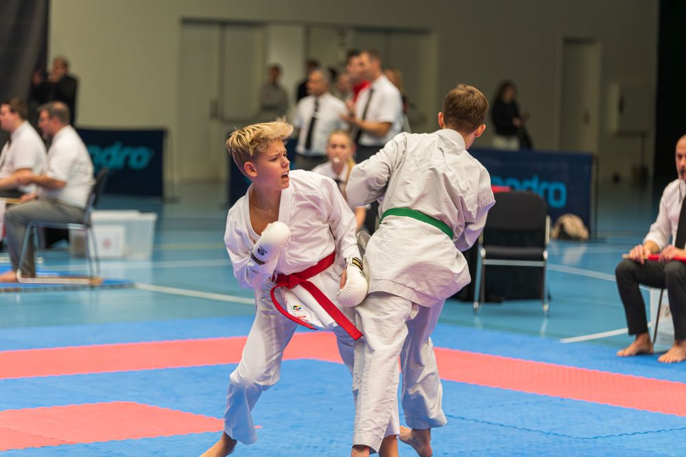 Two young karate students in white gi spar during competitive match on colorful tournament mat.