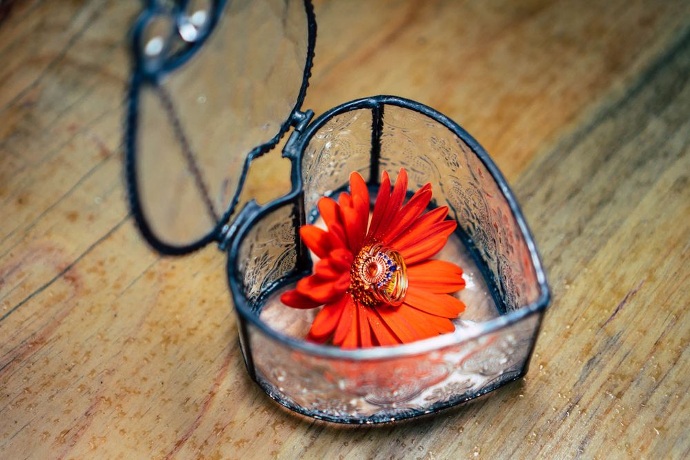A red gerbera daisy flower rests inside a heart-shaped glass pendant necklace on wooden surface.