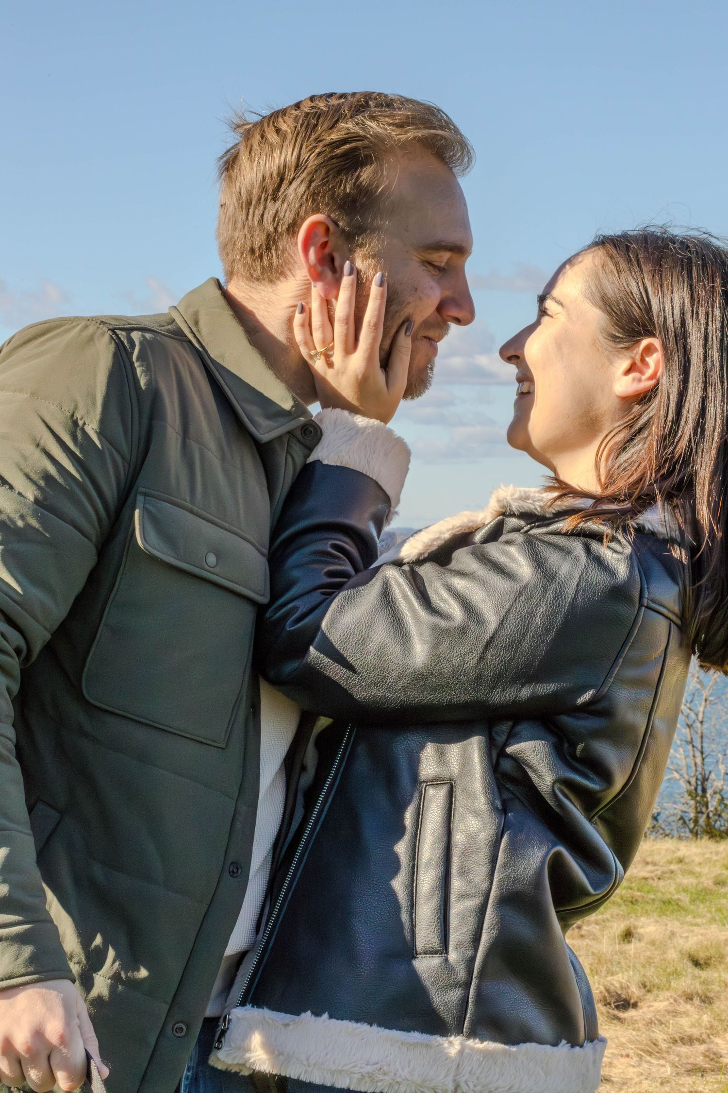 Couple sharing tender moment outdoors against cloudy sky background.
