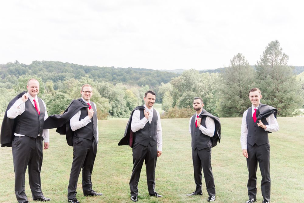 Five groomsmen in matching suits strike playful poses in an outdoor setting.