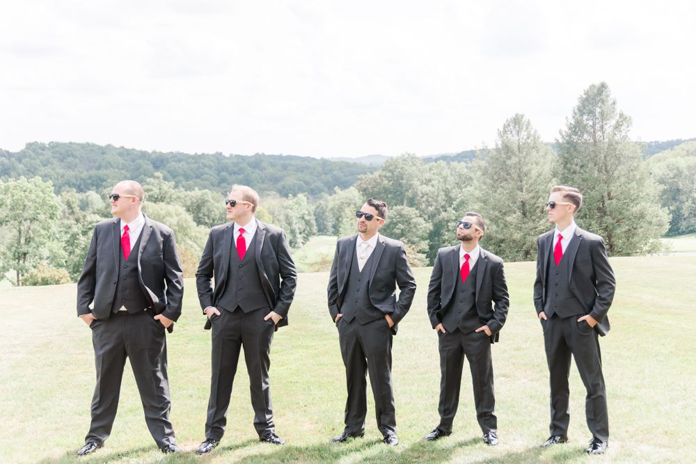 Five men in formal black suits stand confidently on a rolling green hillside.