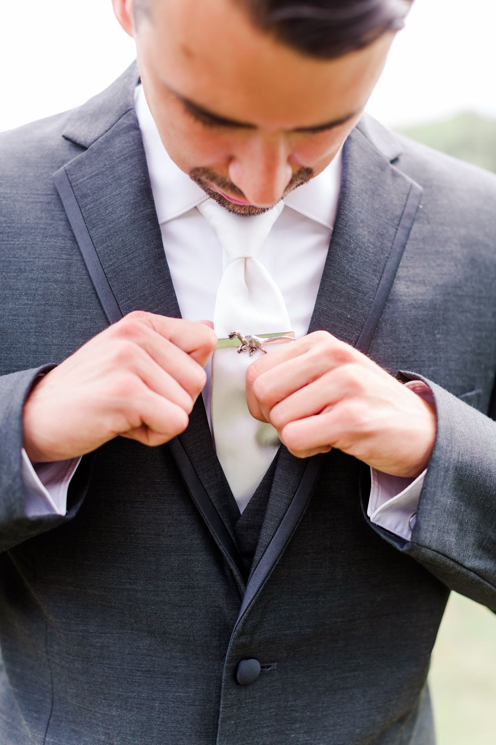 Close-up of groom in grey suit adjusting his tie before the ceremony.
