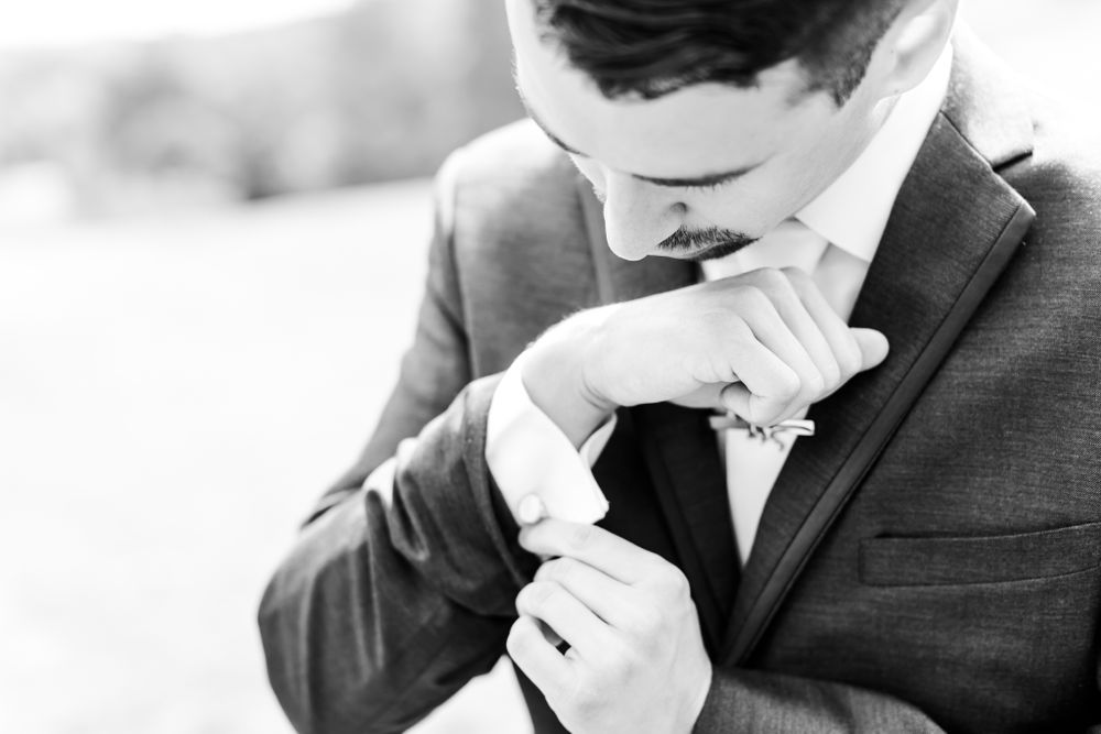 Close-up of groom adjusting his bowtie while smiling.