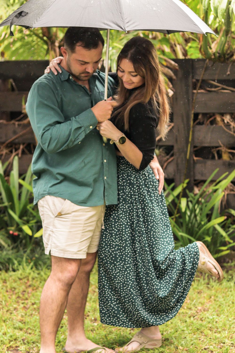 A man and woman hold an umbrella and look at the ground