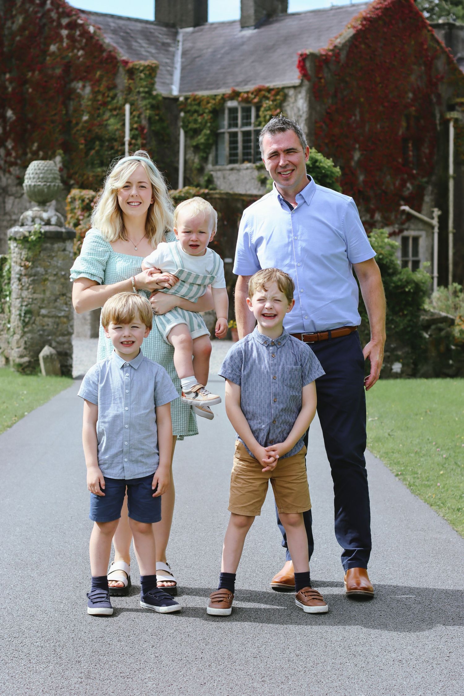 Happy family posing for portrait on path in front of ivy-covered stone house.