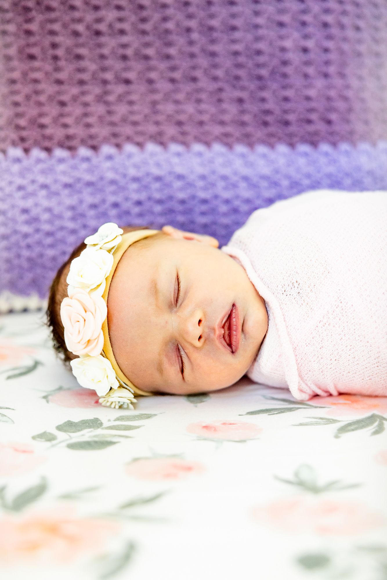 Close up of baby girl's face in flowered headband in her crib during newborn photos in Colorado Springs.