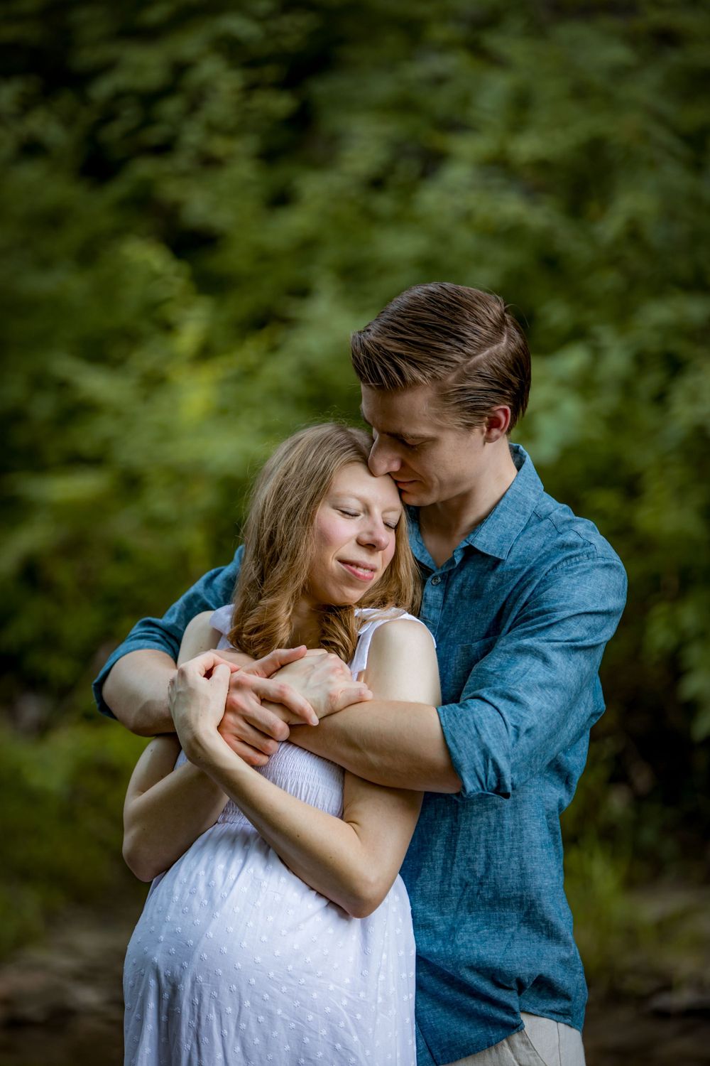 Tender embrace captured in a romantic maternity photo with lush greenery background.