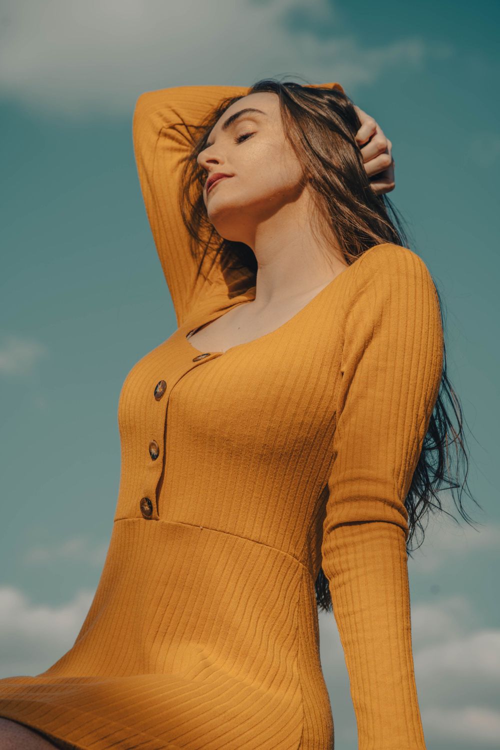 Low angle portrait of woman in fitted yellow dress against blue sky.