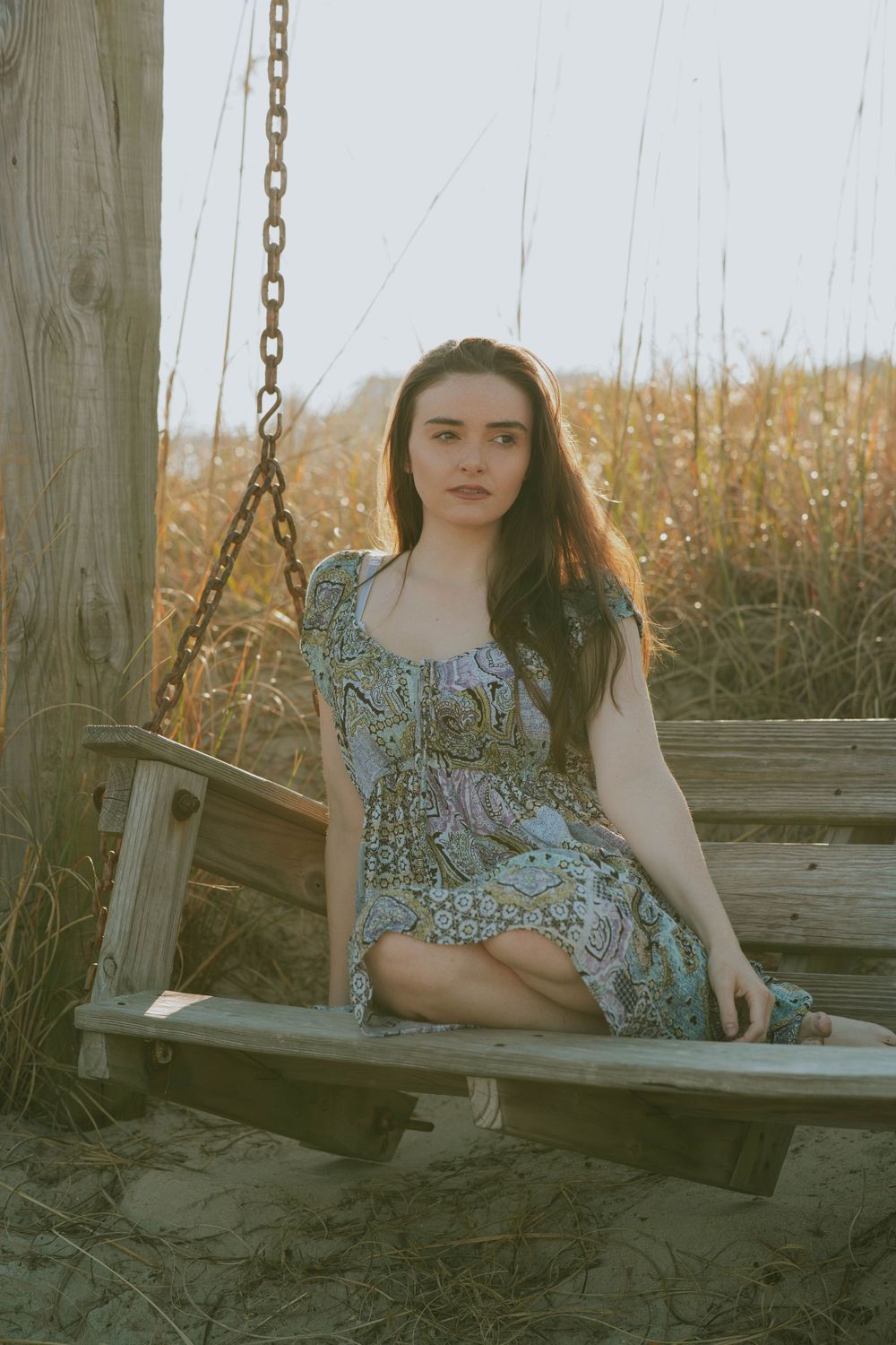 A vintage-style portrait of someone seated on a wooden swing in a field of tall grass.