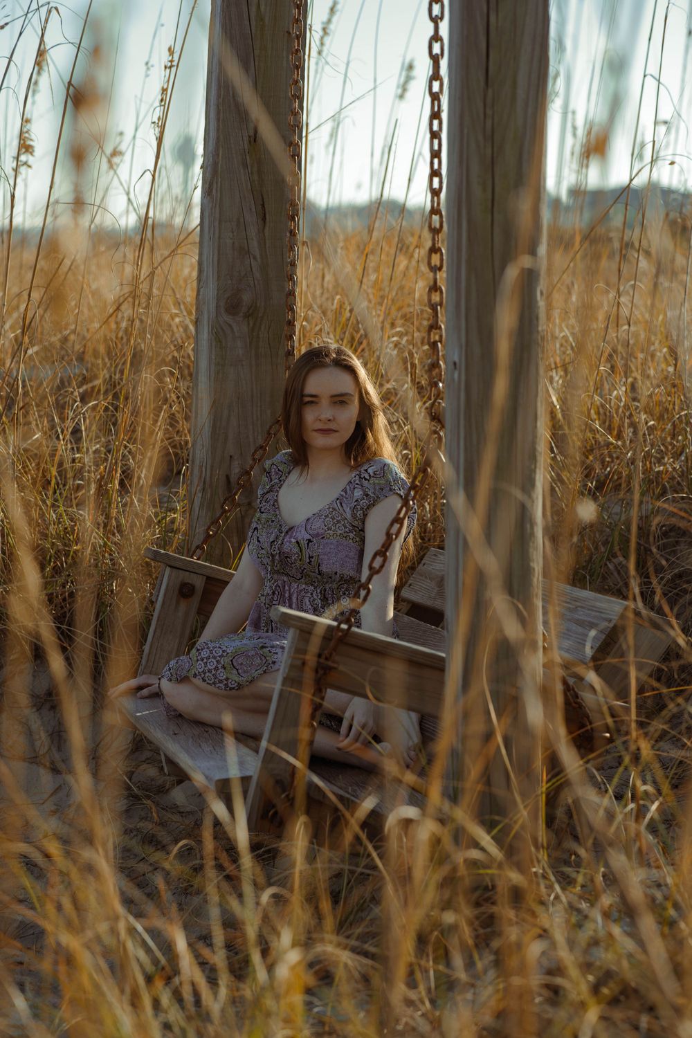 A peaceful moment captured on a wooden swing surrounded by tall golden grass at sunset.