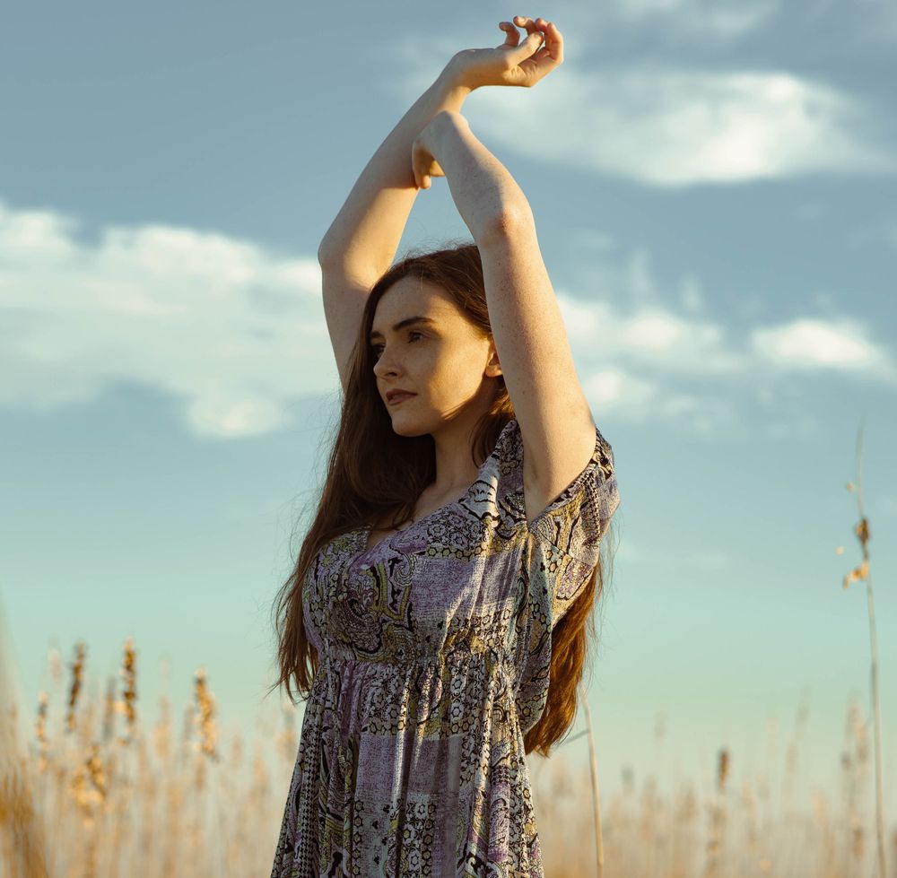 A whimsical pose in a floral dress against a backdrop of golden wheat and blue sky.
