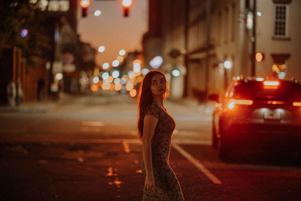 Dramatic nighttime street photography with red taillights and city lighting creating moody ambiance.