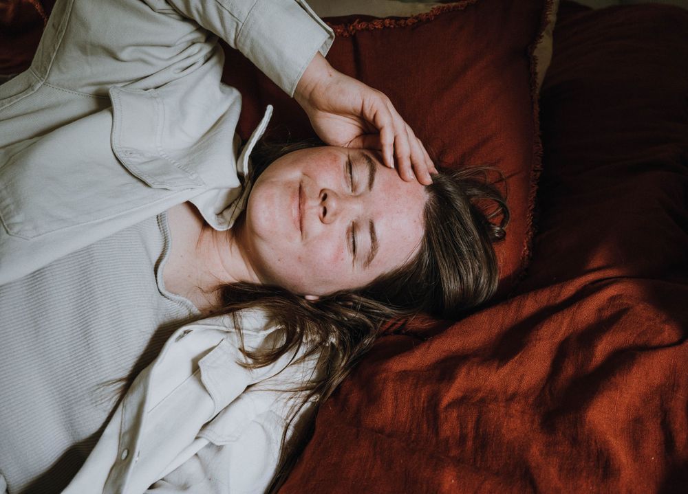 Portrait of a person lying on red bedding with their hand near their face.
