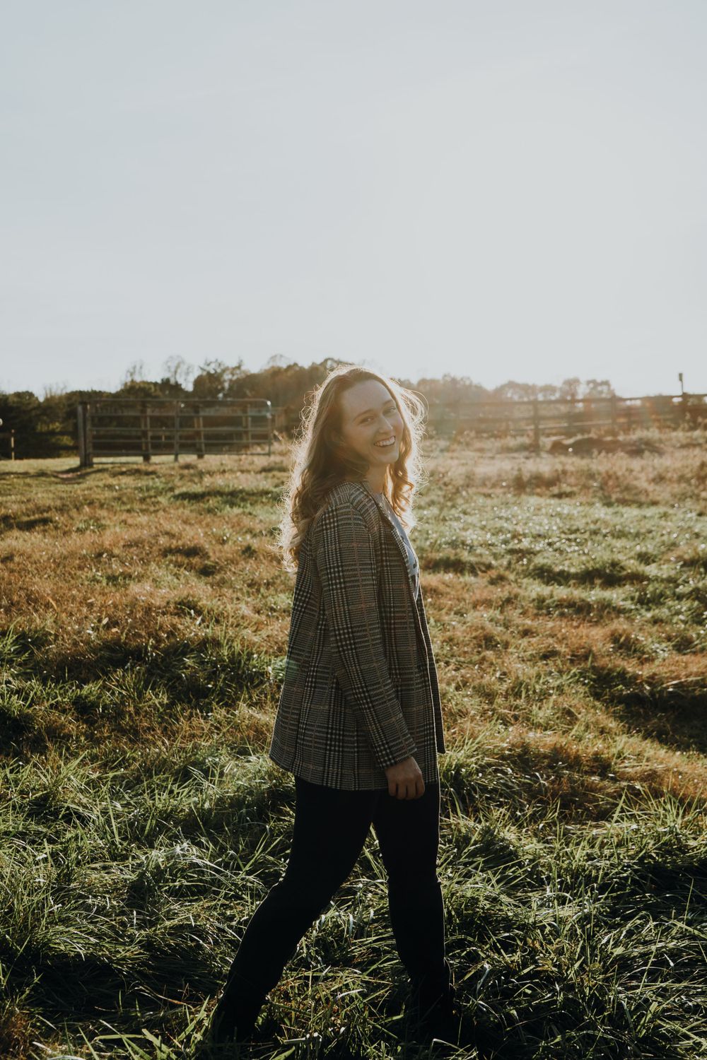 Candid autumn portrait in a plaid blazer walking through a sunlit field.