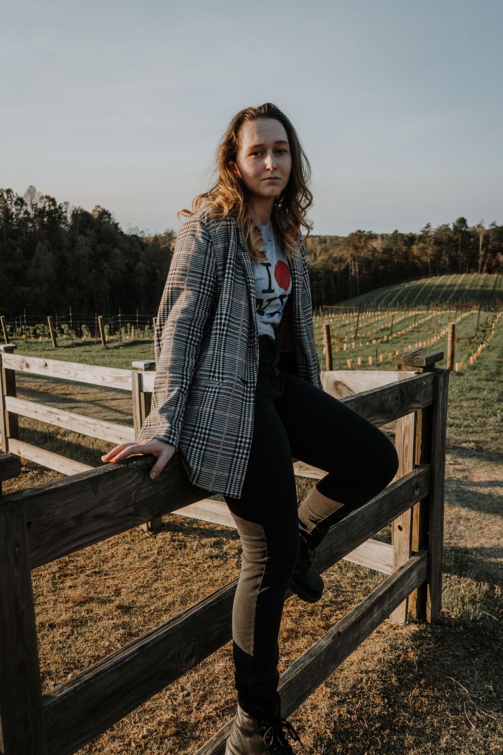 Casual lifestyle portrait sitting on wooden fence at vineyard wearing plaid blazer.