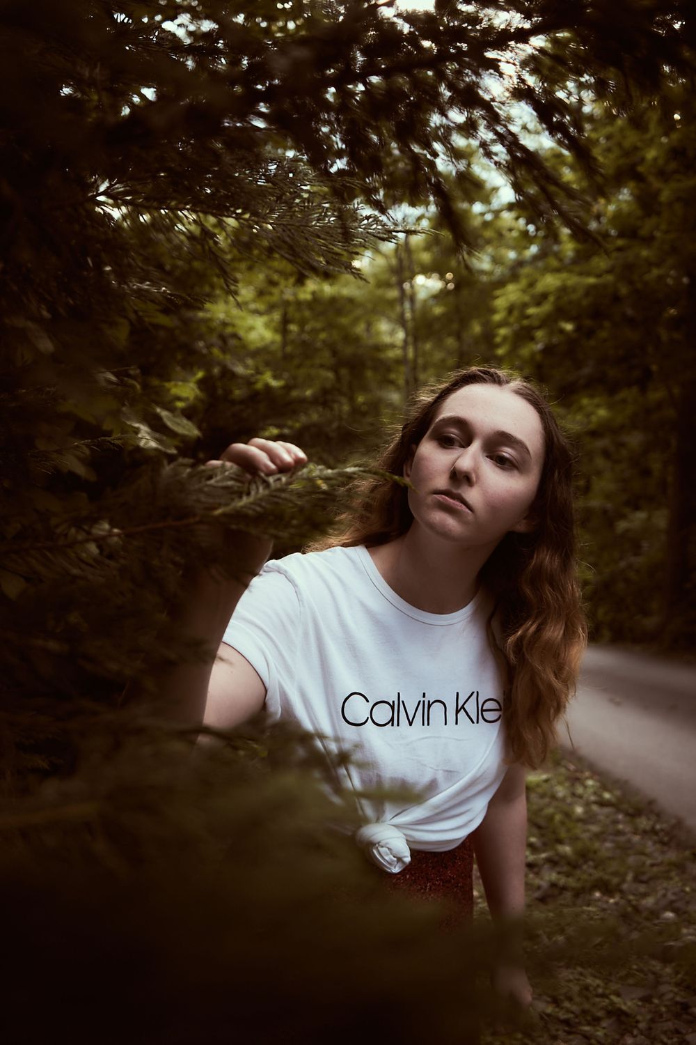 Artistic photo through foliage of person in Calvin Klein shirt on woodland path.