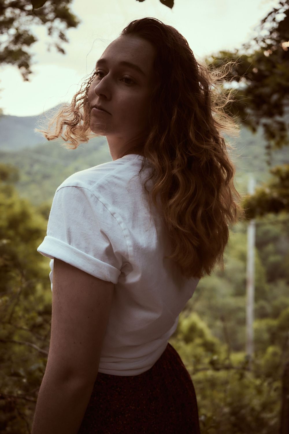 Backlit portrait in white t-shirt against mountain scenery at golden hour.